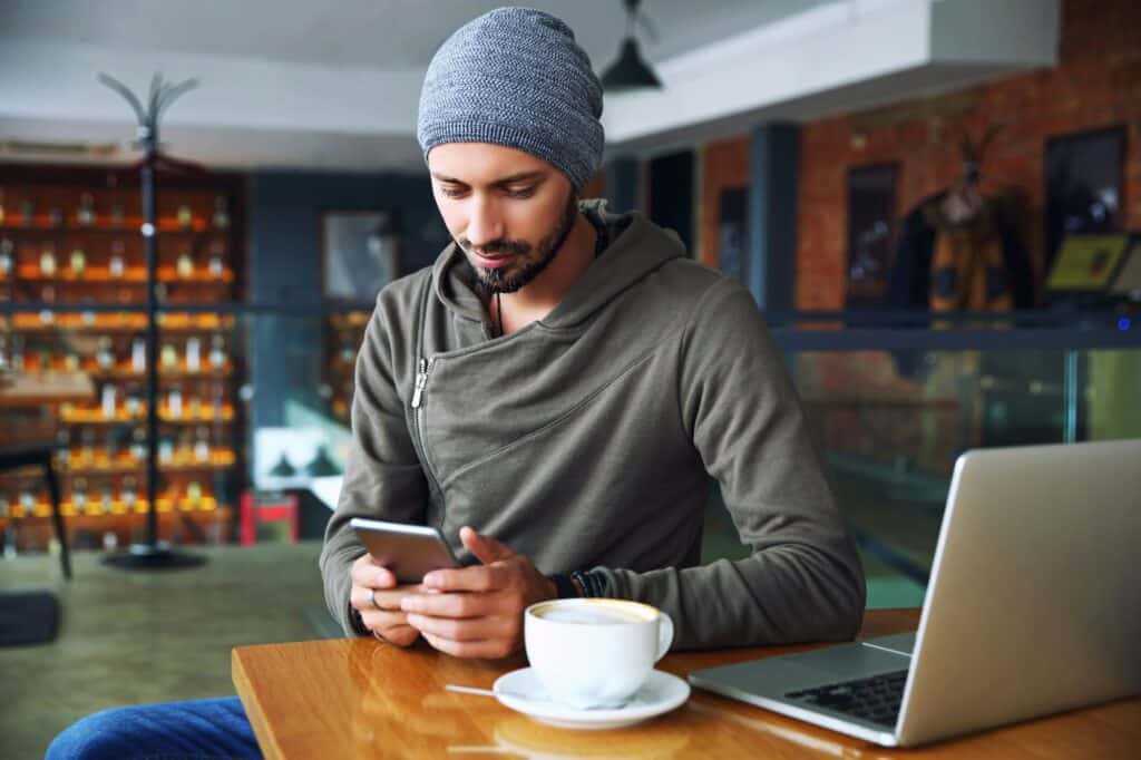 Young handsome hipster guy at the restaurant using a mobile phone.